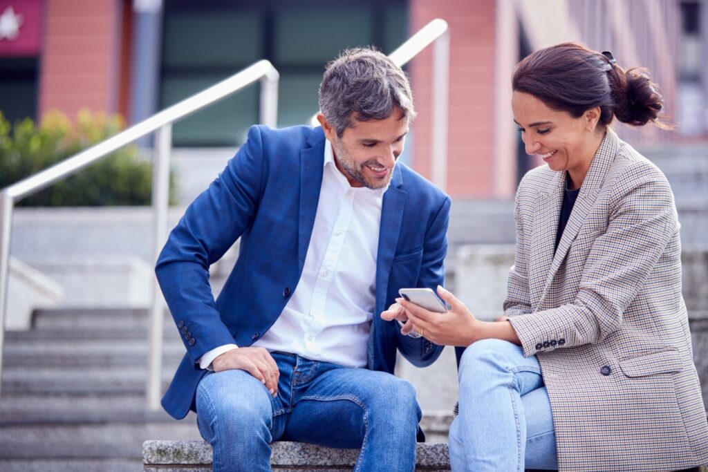 Happy couple sitting by the bench looking at phone