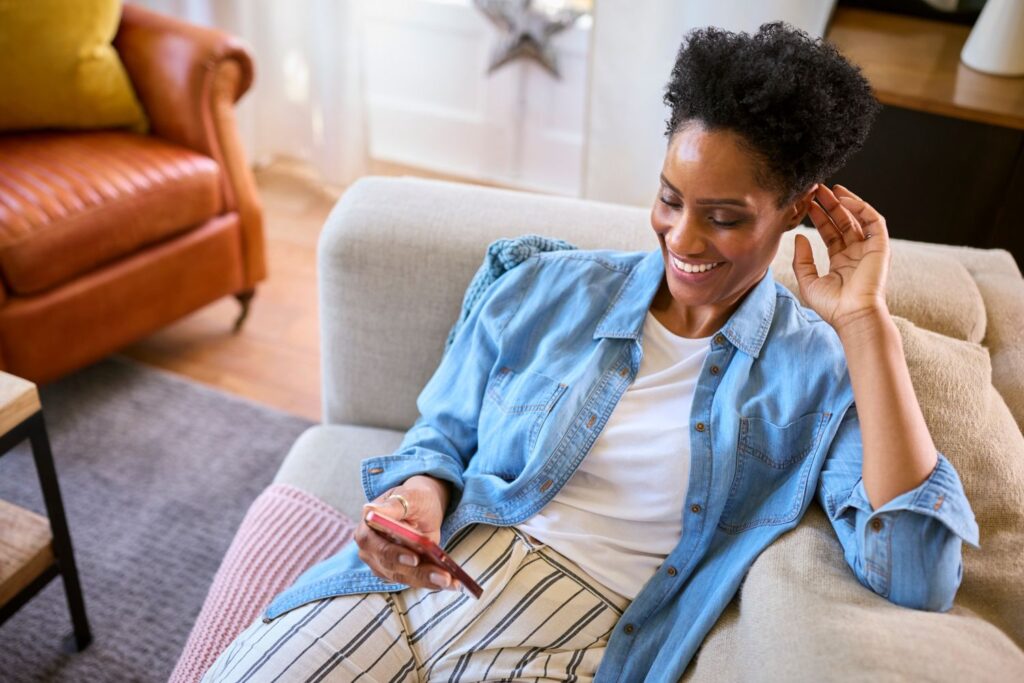 Woman Relaxing On Sofa At Home Looking At Mobile Phone